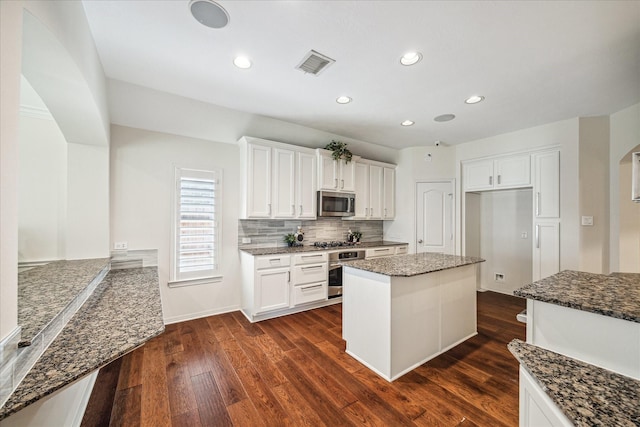 kitchen with visible vents, dark wood finished floors, dark stone counters, stainless steel appliances, and tasteful backsplash