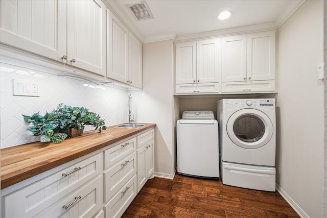 washroom featuring visible vents, washing machine and clothes dryer, cabinet space, a sink, and dark wood-type flooring