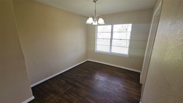 spare room featuring a chandelier, baseboards, and dark wood-style flooring