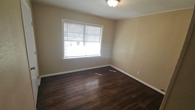 spare room with crown molding, dark wood-type flooring, and baseboards