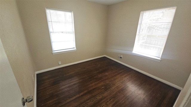 spare room with baseboards and dark wood-style floors