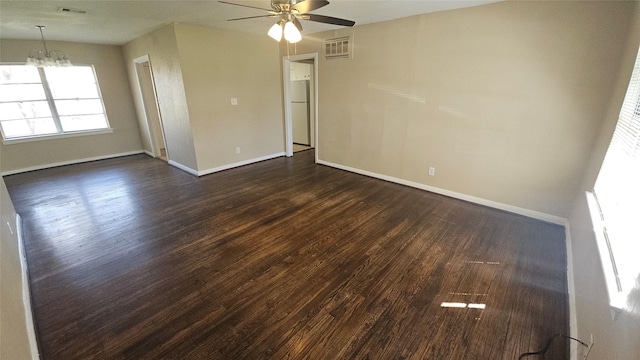 unfurnished room with dark wood-type flooring, ceiling fan with notable chandelier, visible vents, and baseboards