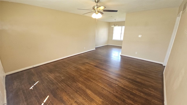 empty room with baseboards, dark wood-type flooring, and ceiling fan with notable chandelier