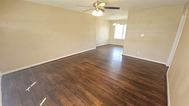 empty room featuring baseboards, dark wood-style flooring, and ceiling fan with notable chandelier