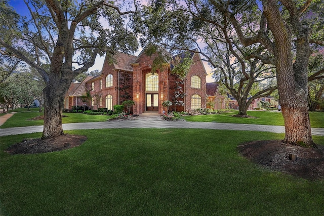 view of front of home featuring a front lawn, french doors, brick siding, and curved driveway