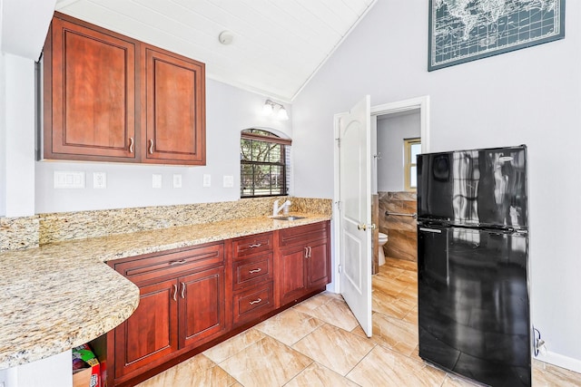 kitchen featuring light stone counters, freestanding refrigerator, a sink, vaulted ceiling, and dark brown cabinets