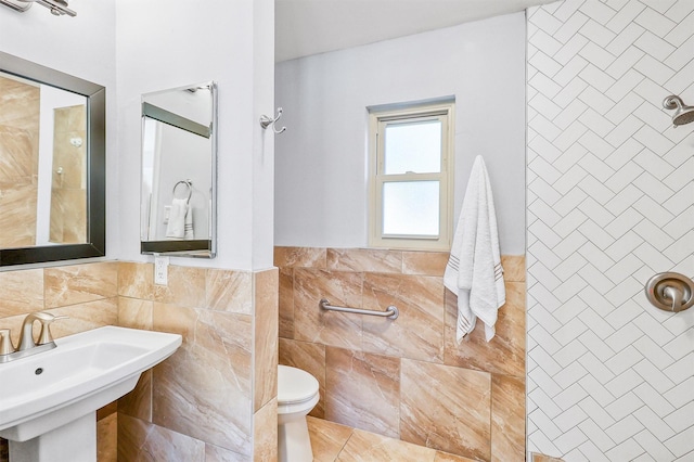 bathroom with a sink, toilet, tile walls, and a tile shower