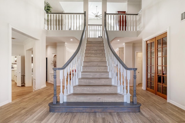 staircase with a high ceiling, wood finished floors, baseboards, and ornamental molding