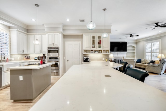 kitchen with light wood finished floors, a center island, open floor plan, ornamental molding, and a ceiling fan