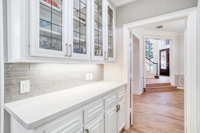 interior space with visible vents, glass insert cabinets, ornamental molding, light wood-style floors, and white cabinetry