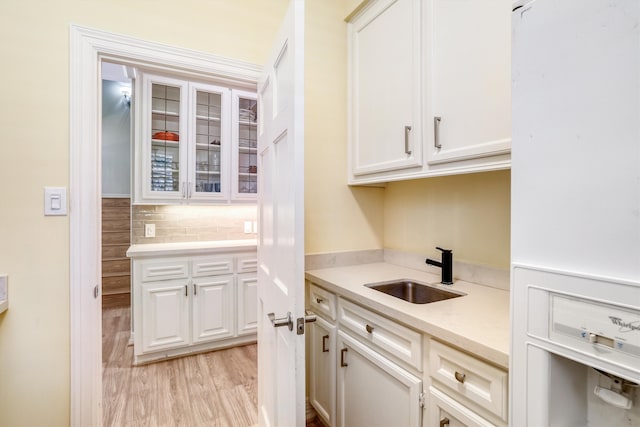 kitchen with light wood-style flooring, a sink, light countertops, white cabinets, and glass insert cabinets