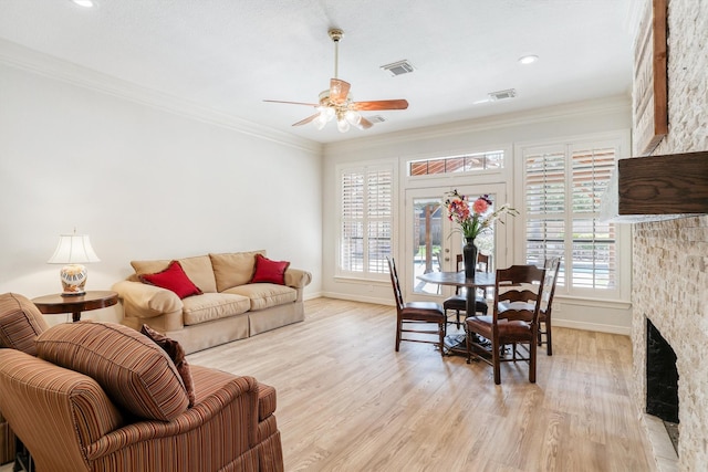 living room with a ceiling fan, visible vents, light wood-style flooring, a fireplace, and ornamental molding