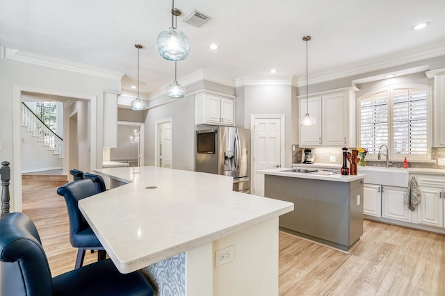 kitchen with visible vents, a sink, a kitchen island, stainless steel fridge with ice dispenser, and decorative backsplash