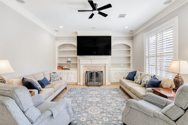 living area featuring visible vents, a fireplace, ceiling fan, light wood-style floors, and crown molding