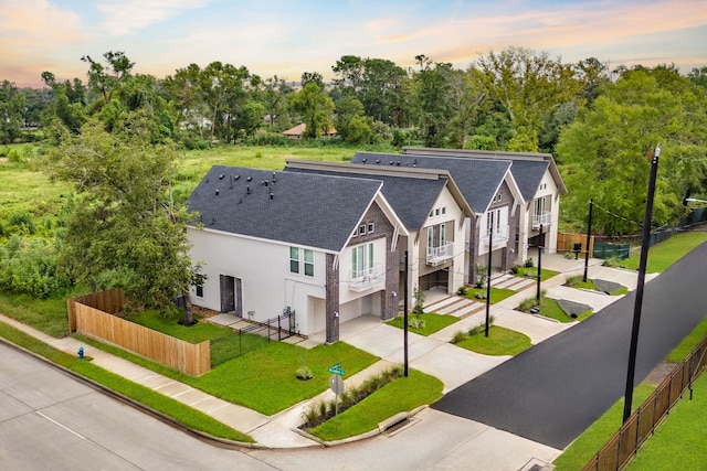 view of front of property with driveway, roof with shingles, a front yard, a garage, and fence private yard