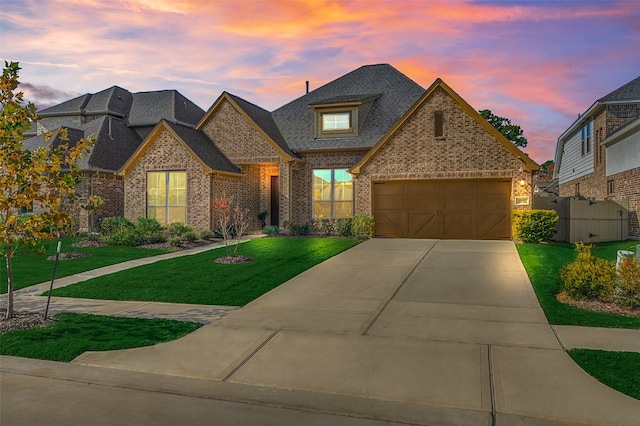 french country home with a lawn, concrete driveway, an attached garage, a shingled roof, and brick siding