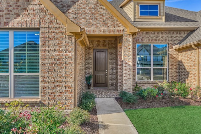 entrance to property with brick siding and a shingled roof