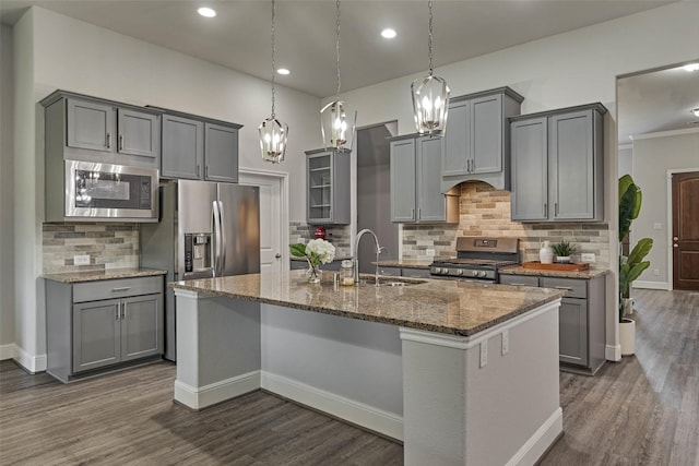 kitchen featuring gray cabinetry, a center island with sink, a sink, dark stone countertops, and appliances with stainless steel finishes