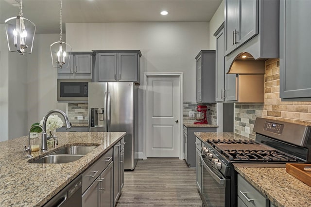 kitchen featuring gray cabinets, a sink, light stone counters, wood finished floors, and appliances with stainless steel finishes