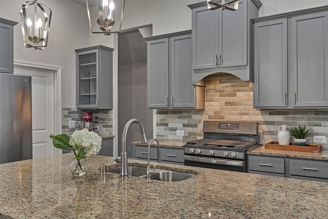 kitchen with gray cabinetry, a sink, backsplash, appliances with stainless steel finishes, and light stone countertops