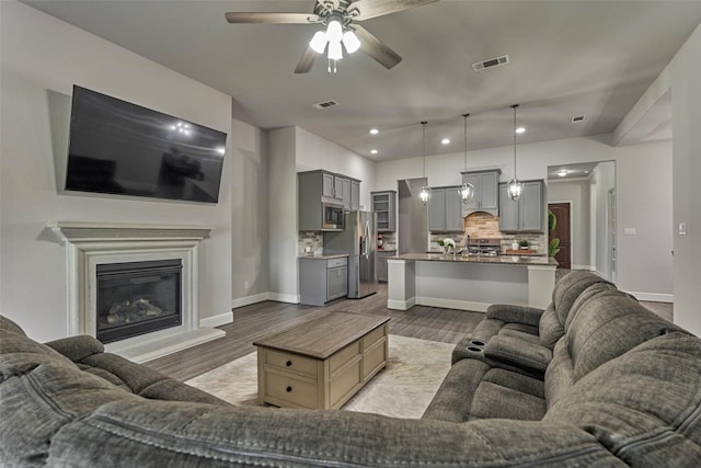 living room featuring light wood-style flooring, visible vents, and ceiling fan