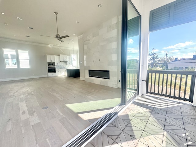 unfurnished living room featuring light wood finished floors, baseboards, ornamental molding, a tile fireplace, and a ceiling fan