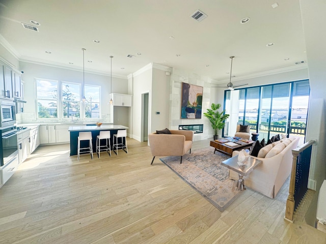 living area featuring visible vents, a large fireplace, light wood-style floors, and crown molding