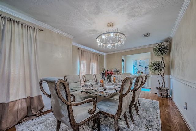 dining room with visible vents, ornamental molding, a textured ceiling, wood finished floors, and an inviting chandelier