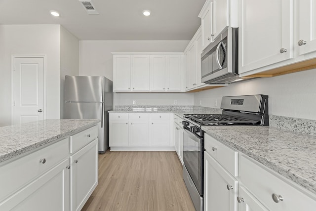 kitchen featuring visible vents, white cabinetry, stainless steel appliances, light wood-style floors, and light stone countertops