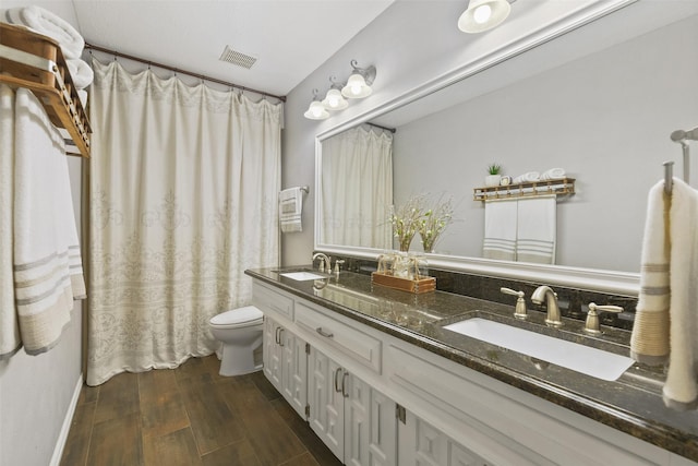 bathroom featuring toilet, wood finished floors, visible vents, and a sink