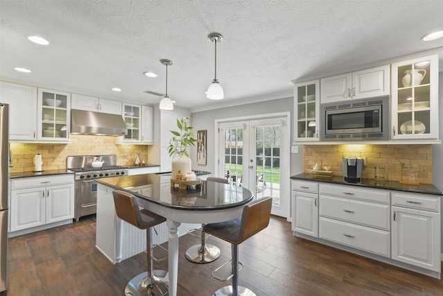 kitchen featuring under cabinet range hood, stainless steel appliances, dark countertops, and a breakfast bar