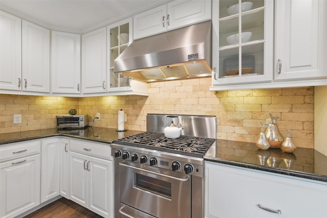 kitchen featuring under cabinet range hood, white cabinets, dark stone counters, and stainless steel stove