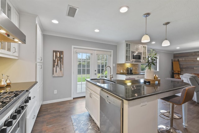 kitchen featuring visible vents, a sink, appliances with stainless steel finishes, wall chimney exhaust hood, and crown molding