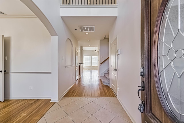 foyer entrance with visible vents, ceiling fan, stairs, arched walkways, and light tile patterned flooring