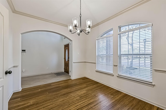 spare room with crown molding, a notable chandelier, wood finished floors, and arched walkways