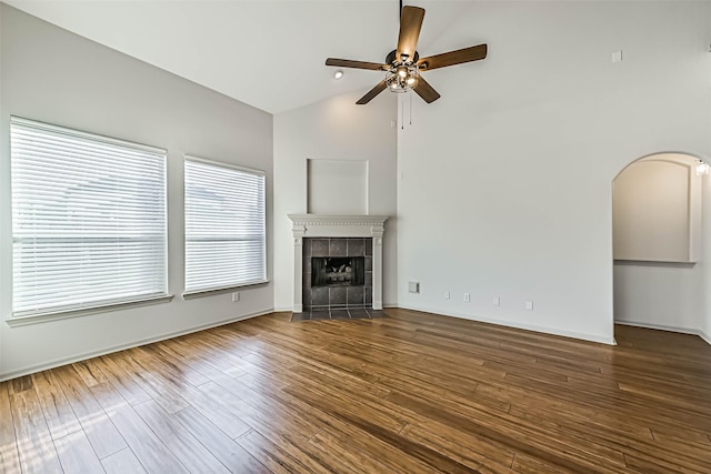 unfurnished living room featuring arched walkways, wood finished floors, a ceiling fan, and a tile fireplace