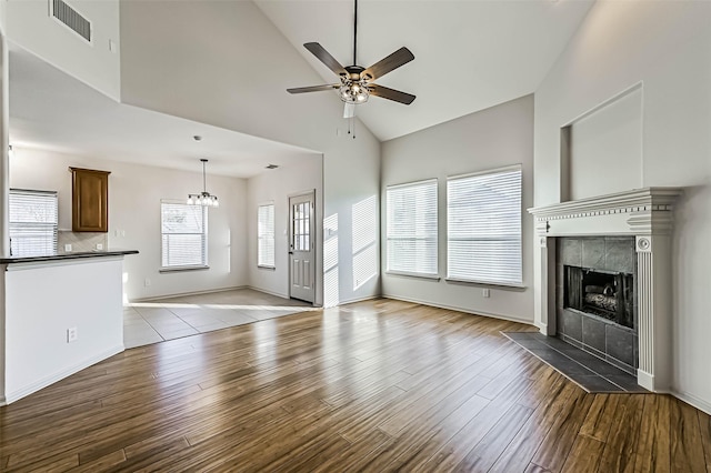 unfurnished living room with visible vents, ceiling fan with notable chandelier, a fireplace, wood finished floors, and high vaulted ceiling