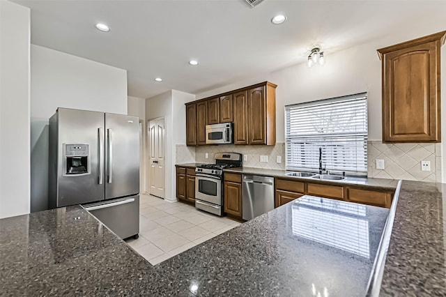 kitchen with a sink, dark stone countertops, appliances with stainless steel finishes, light tile patterned floors, and decorative backsplash