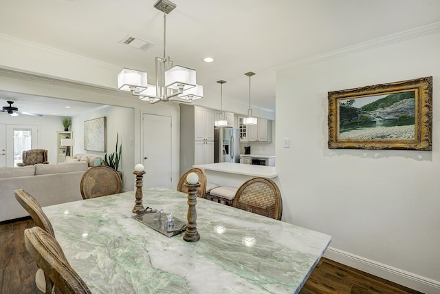 dining area featuring visible vents, ceiling fan with notable chandelier, dark wood finished floors, crown molding, and baseboards