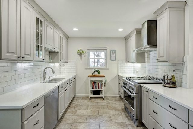 kitchen with a sink, light countertops, glass insert cabinets, appliances with stainless steel finishes, and wall chimney exhaust hood