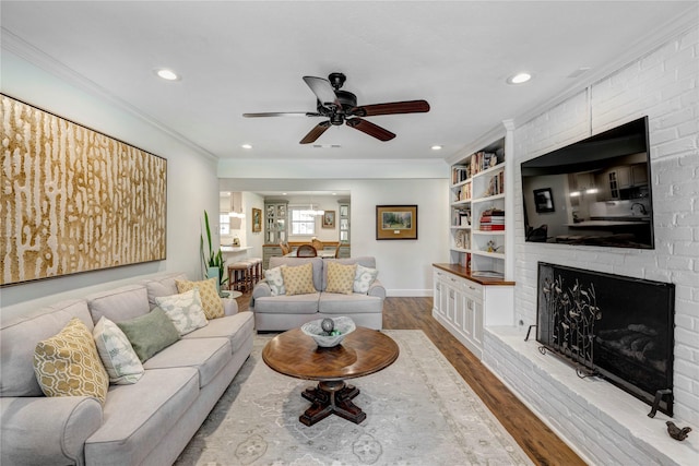 living area with ornamental molding, wood finished floors, recessed lighting, a brick fireplace, and ceiling fan