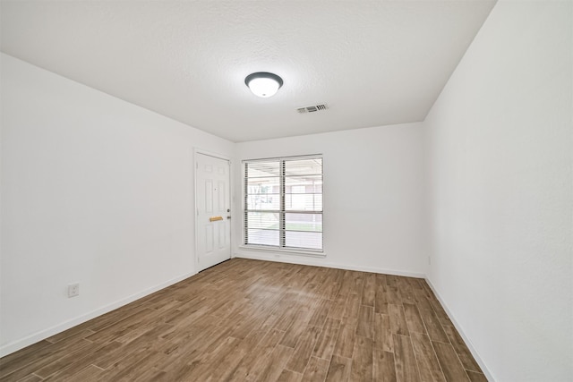 empty room with visible vents, baseboards, a textured ceiling, and wood finished floors