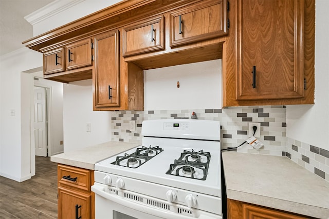 kitchen with brown cabinets, light countertops, crown molding, white gas range, and backsplash