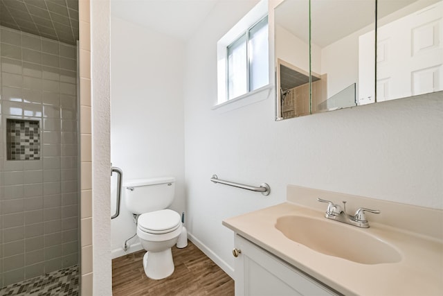 full bathroom with baseboards, toilet, tiled shower, wood finished floors, and vanity