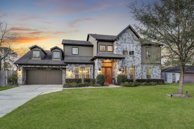 view of front facade featuring an attached garage, a shingled roof, a yard, stone siding, and driveway