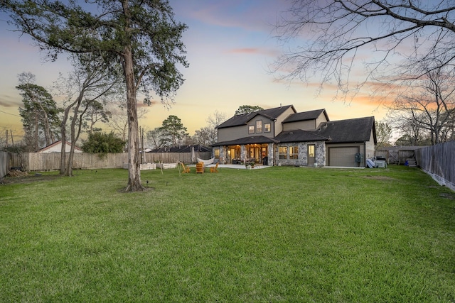 back of property at dusk with an attached garage, a fenced backyard, and a yard