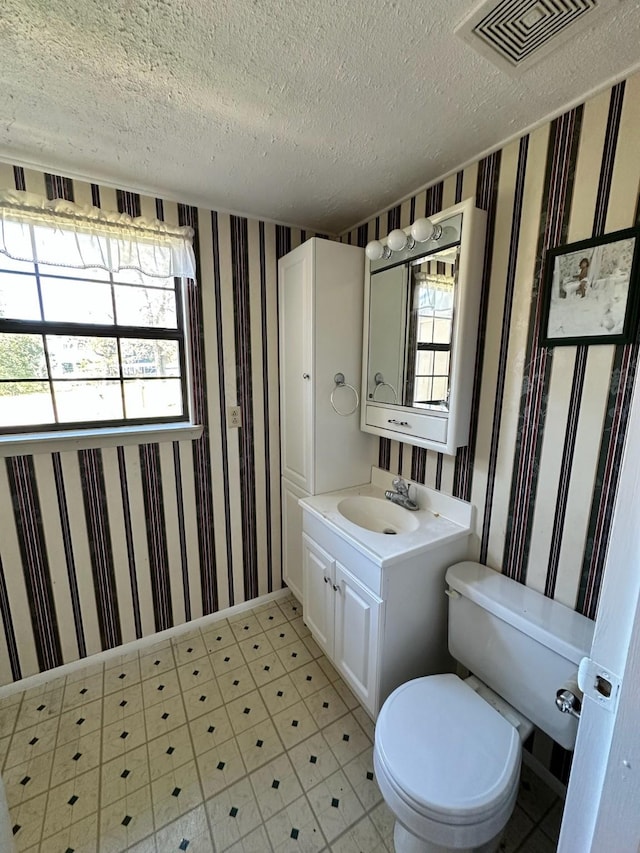 bathroom featuring visible vents, wallpapered walls, toilet, tile patterned floors, and a textured ceiling