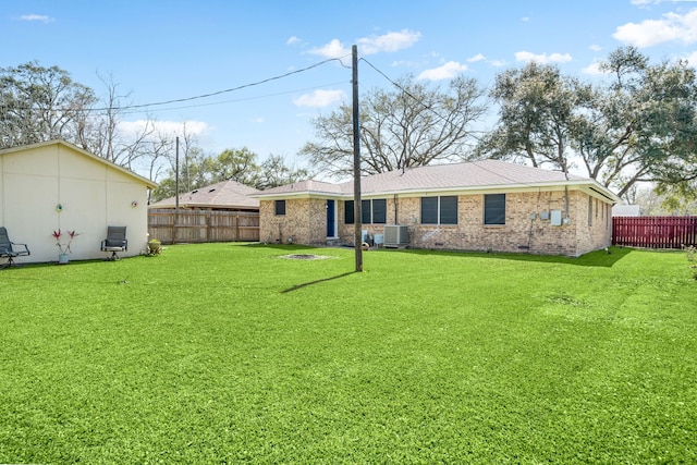 back of house featuring brick siding, a fenced backyard, cooling unit, and a yard