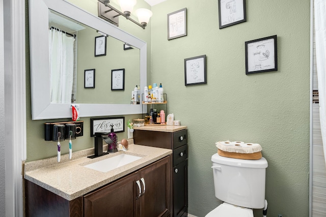 bathroom with vanity, toilet, and a textured wall