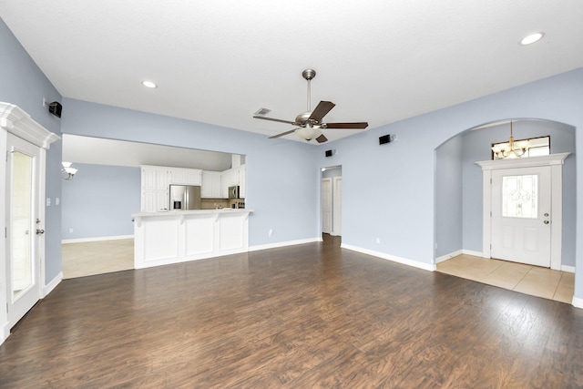 unfurnished living room featuring baseboards, arched walkways, wood finished floors, and ceiling fan with notable chandelier